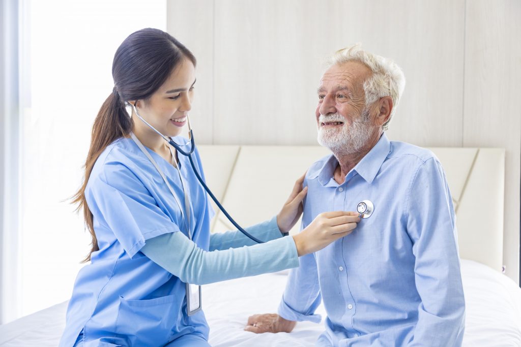 Hospice nurse is using stethoscope on Caucasian man in bed